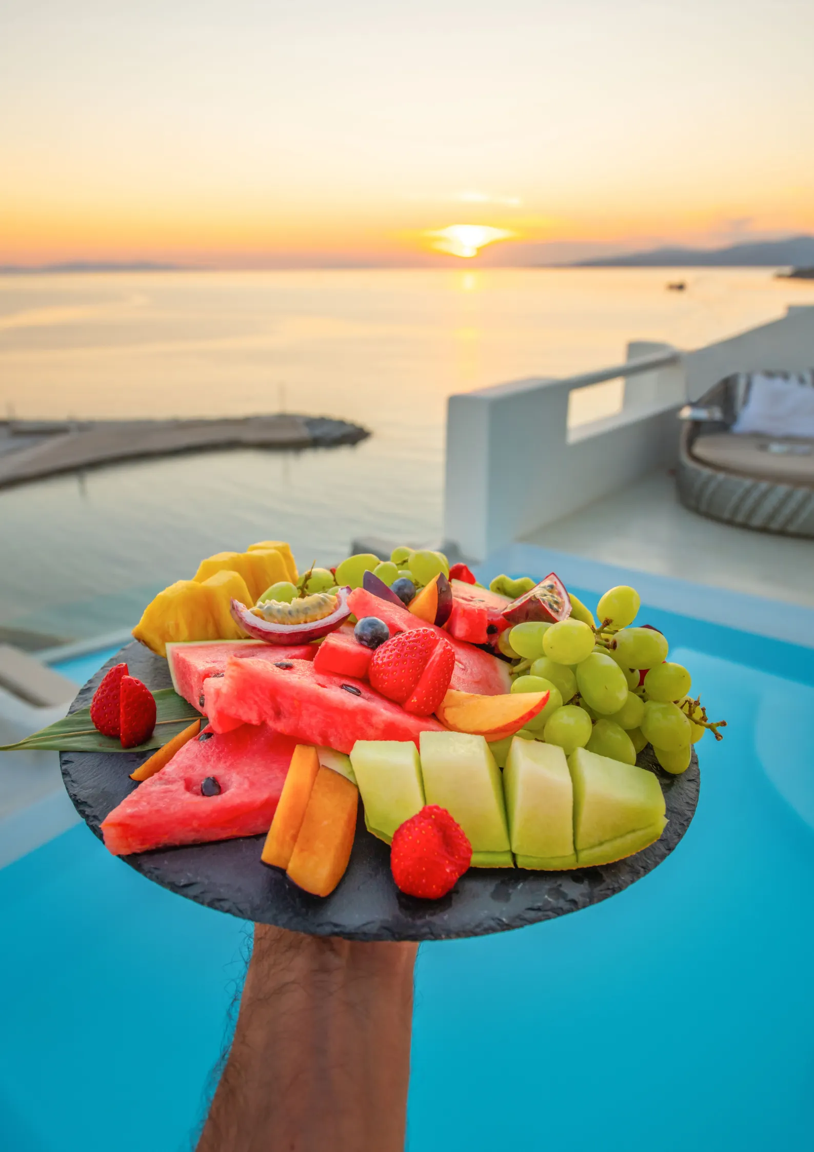 een fruitschaal wordt hoog gehouden boven een overloopzwembad met uitzicht op zee