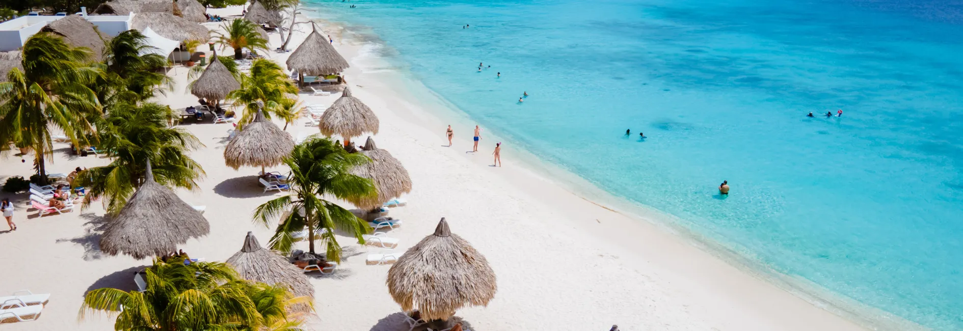 Vogelperspectief van tropisch wit zandstrand met palmbomen en ligbedden en helderblauwe zee 