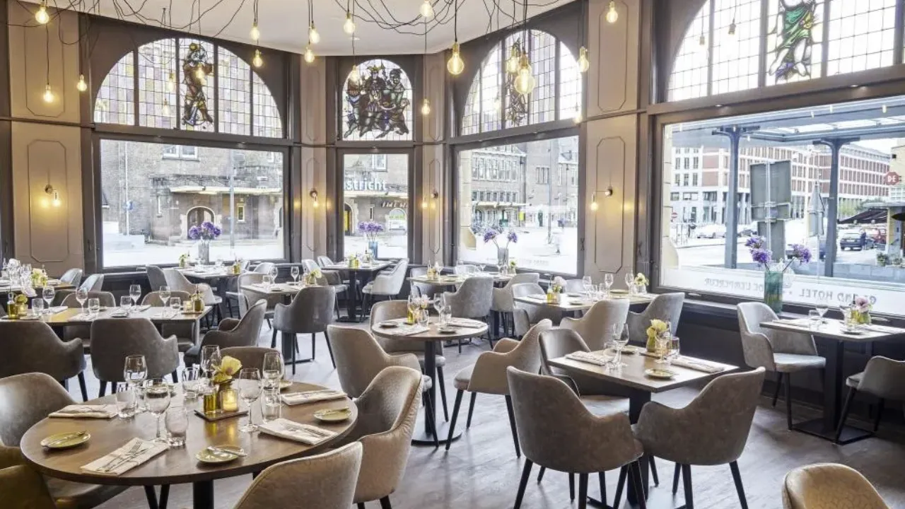 Eetzaal in Amrâth Grand Hotel lEmpereur met grijze stoelen en uitzicht op de winkelstraat in Maastricht