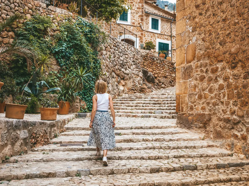 Vrouw loopt een trap op in Palma de Mallorca, omringd door huizen van natuursteen en planten