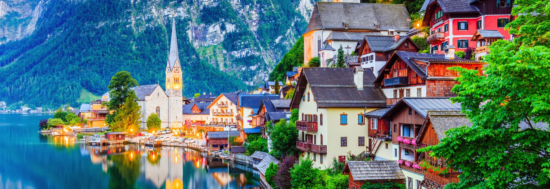Dorp aan een meer met een kerktoren en huizen waar de lichten aanstaan en bergen op de achtergrond
