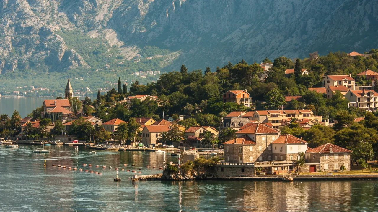 Oranje/rode huizen omringd met bossen en aan het water met op de achtergrond bergen
