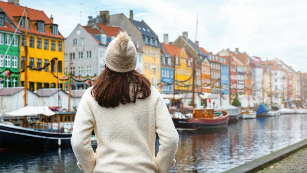 Vrouw in winterkleding voor gekleurde huisjes aan kanaal met boten