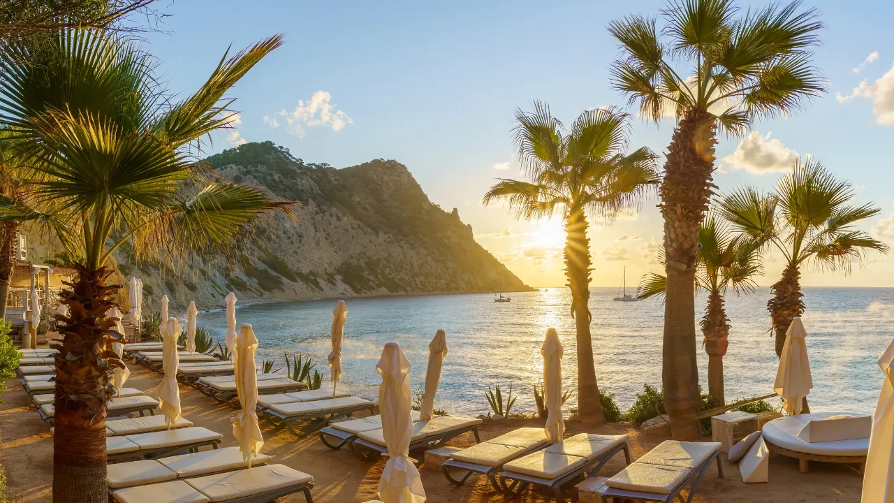 Strand met ondergaande zon met ligbedjes en palmbomen met uitzicht over zee en rots