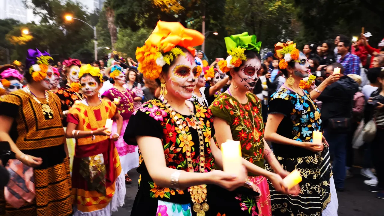 Groep mensen geschminkt met kleurrijke kleding aan en kaarsen in hun handen wandelen in een optocht