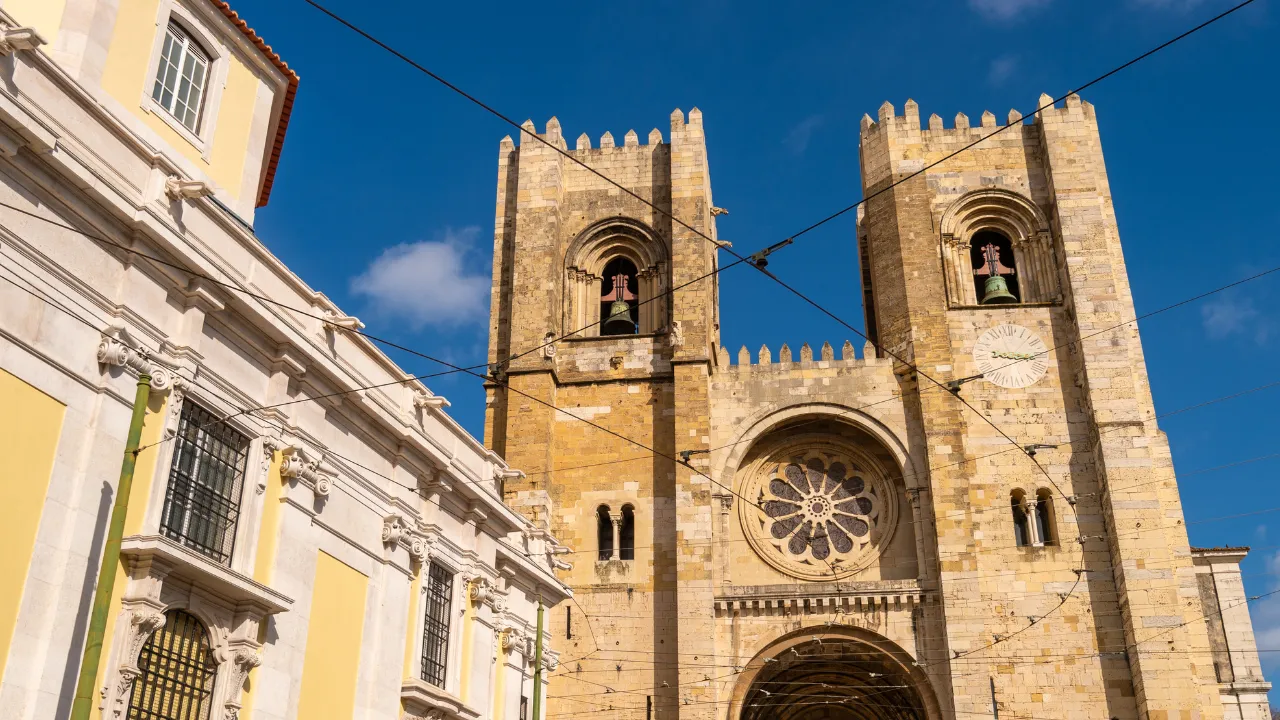 Kathedraal van Lissabon vanonder met blauwe lucht op de achtergrond die contrasteert meer de gele gebouwen