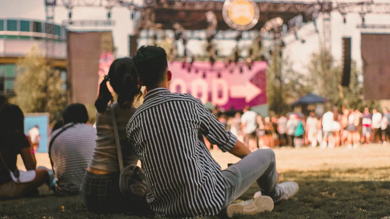 Twee mensen die op festivalterrein zitten met ruggen naar de voorgrond