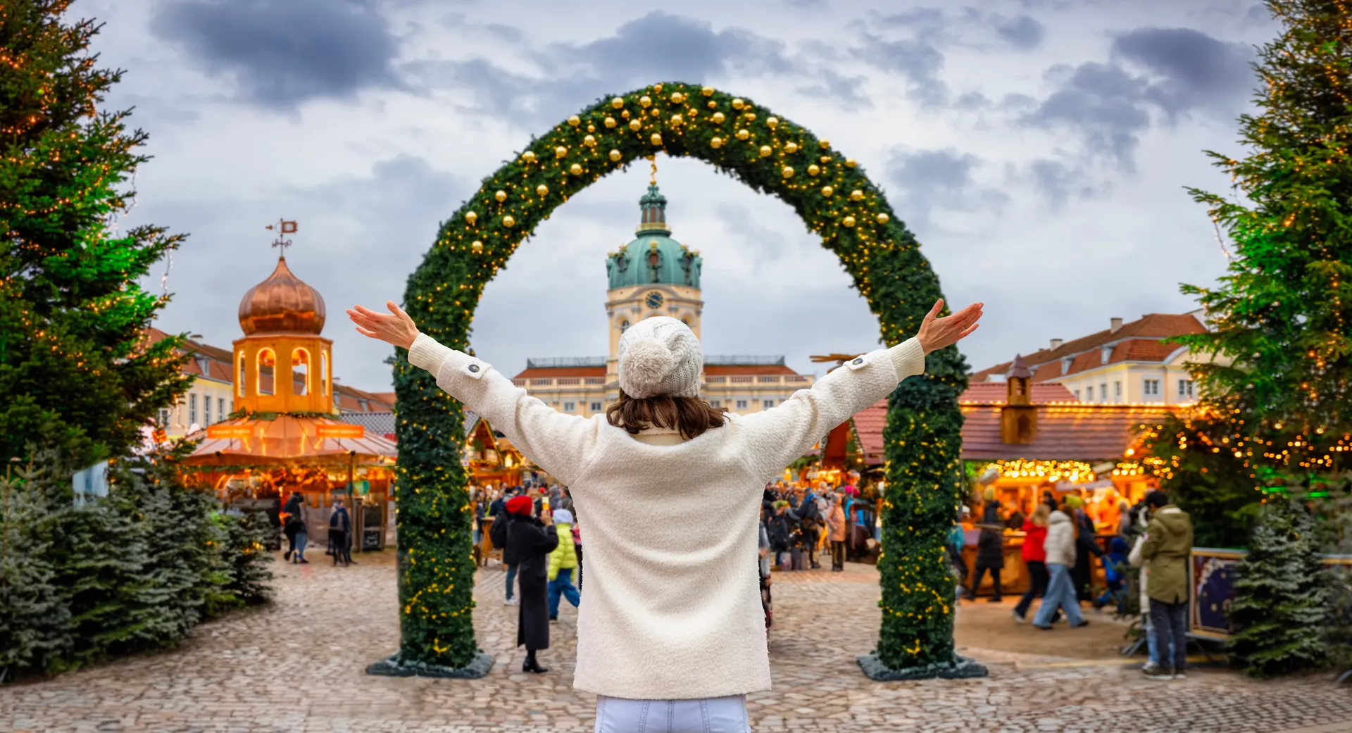Vrouw met gespreide armen voor kerstmarkt met grote boog met kerstversiering