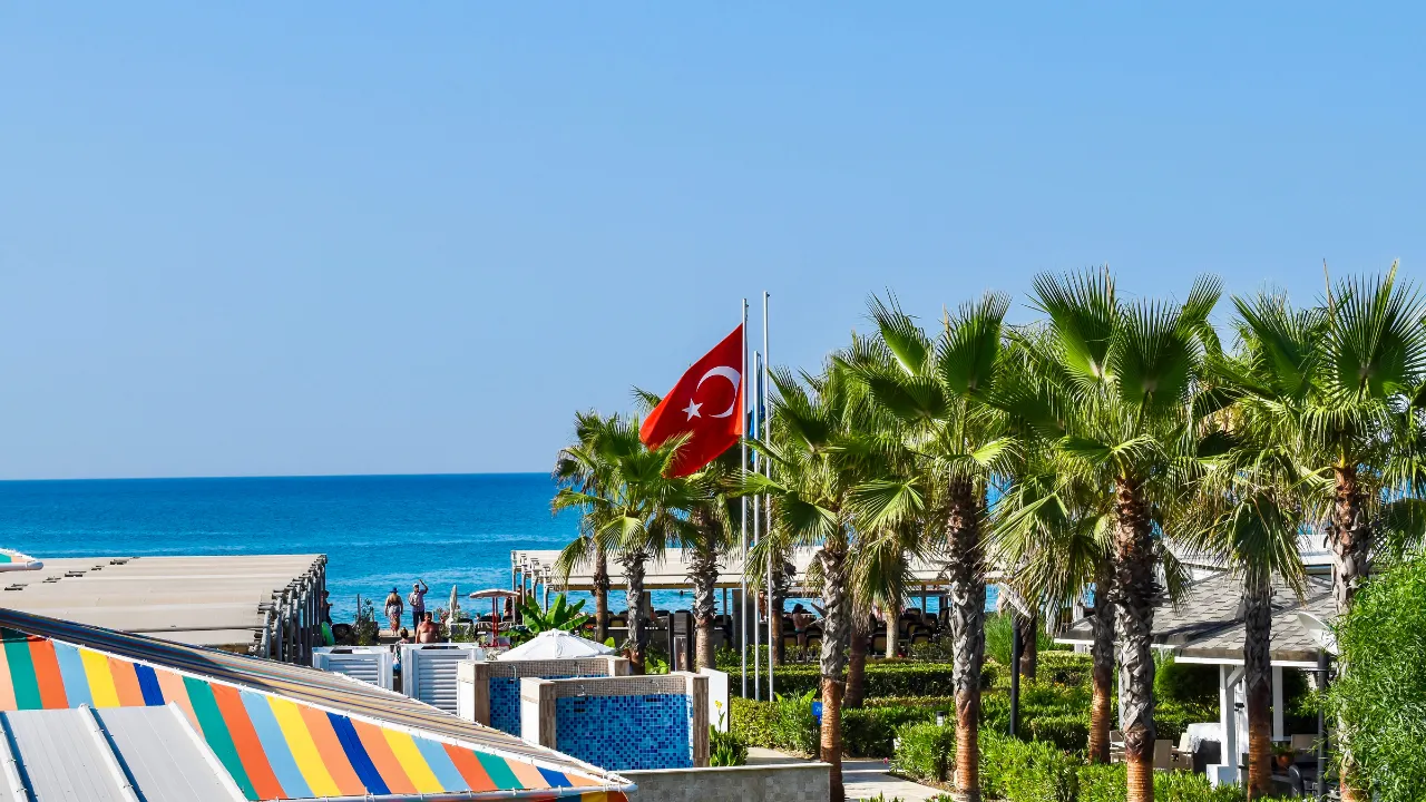 Turkse vlag, palmbomen en paviljoens op het strand van Belek, de zee op de achtergrond