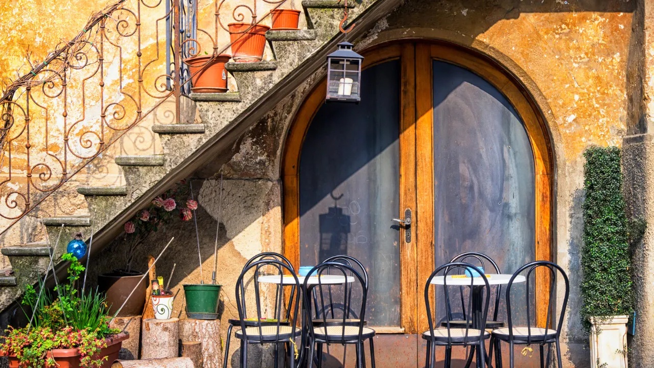 Stoelen en tafeltjes die voor een zwarte deur in een gele muur staan met een stenen trap die schuin omhoog over de deur gaat