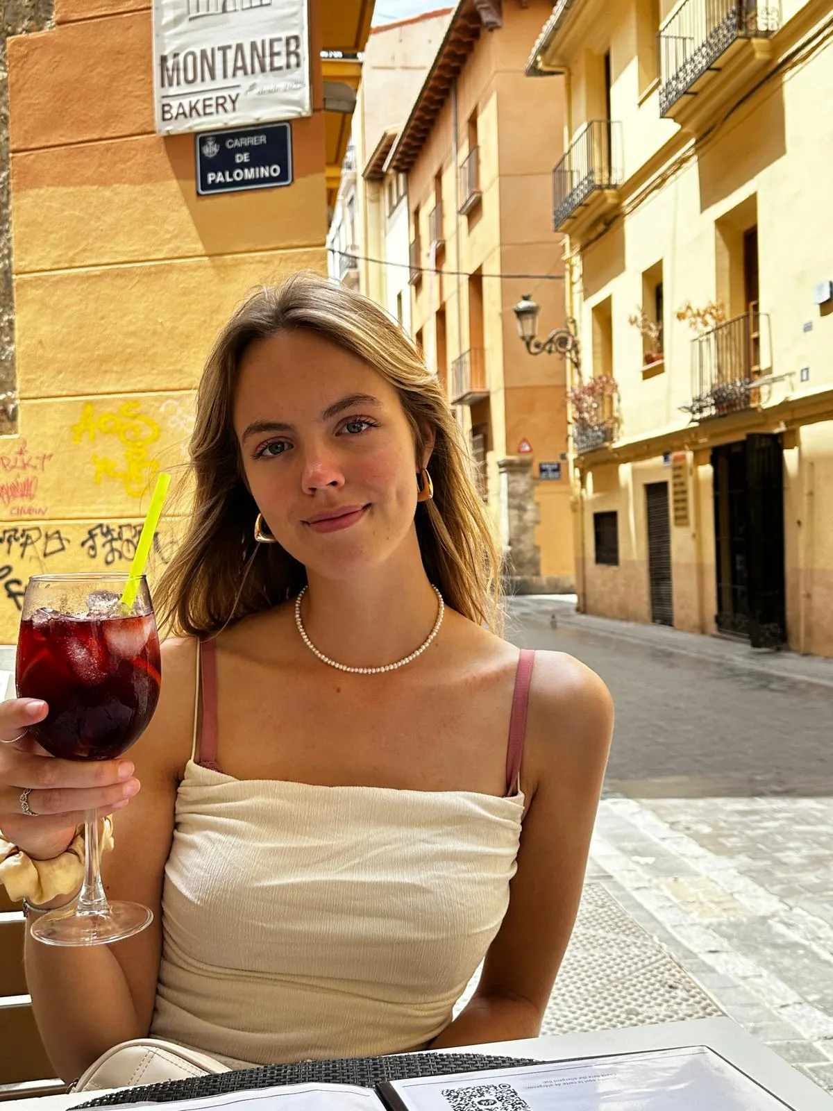 Jonge vrouw zit in een straatcafé en houdt een glas met een roodviolet ...