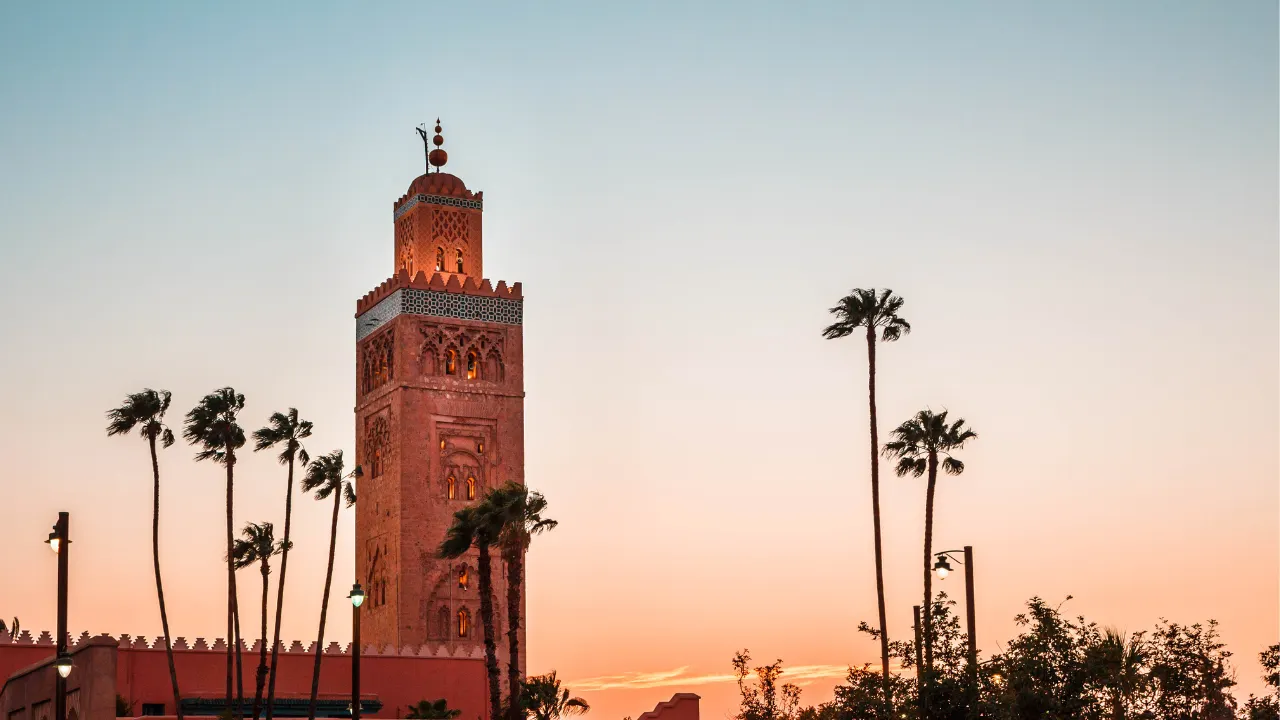 Stad Marrakech met toren en op de achtergrond oranje-blauwe lucht en palmbomen 