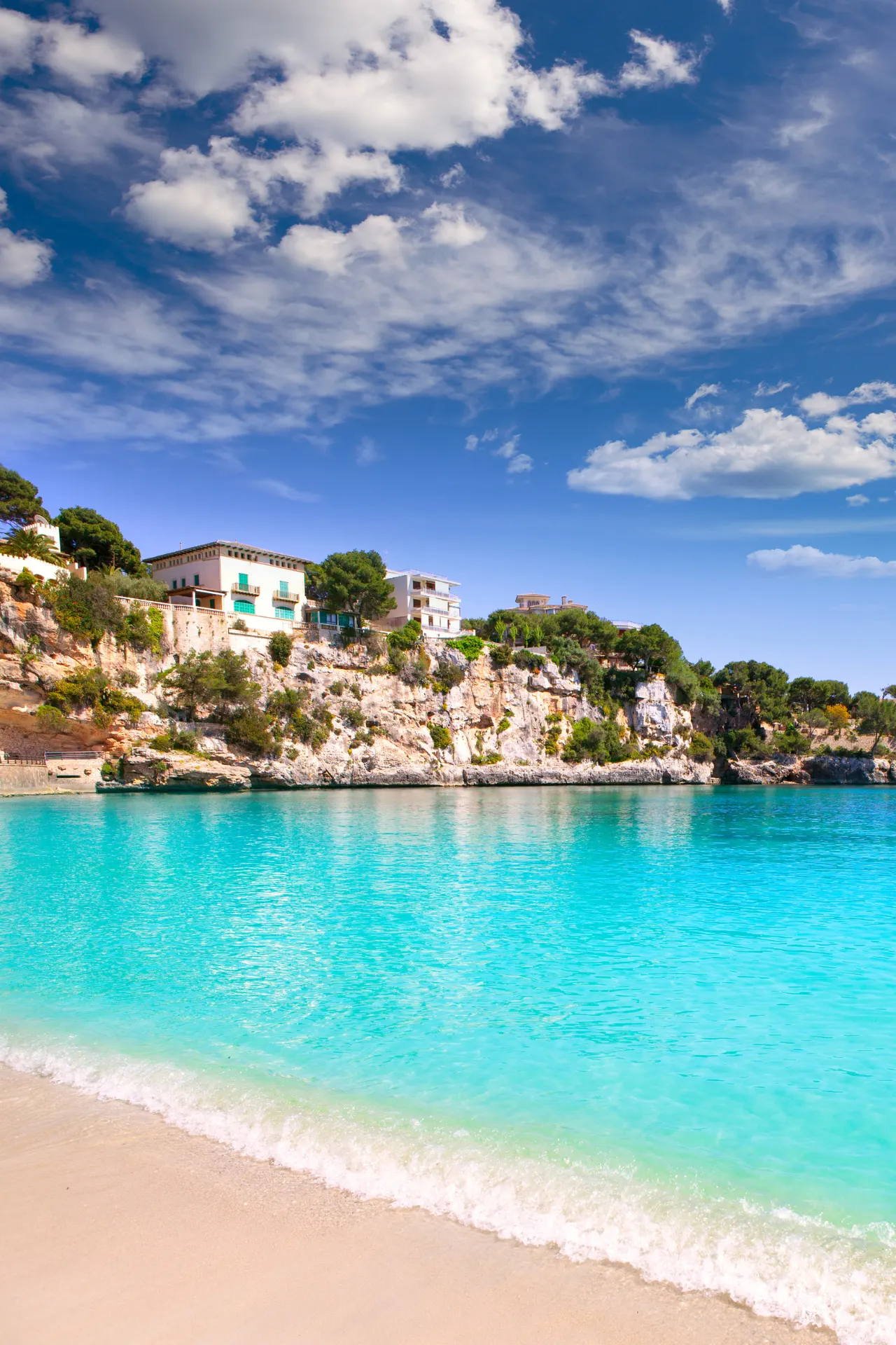 Ondiep strand, turquoise water en de kust van Mallorca met bomen en huizen op de achtergrond