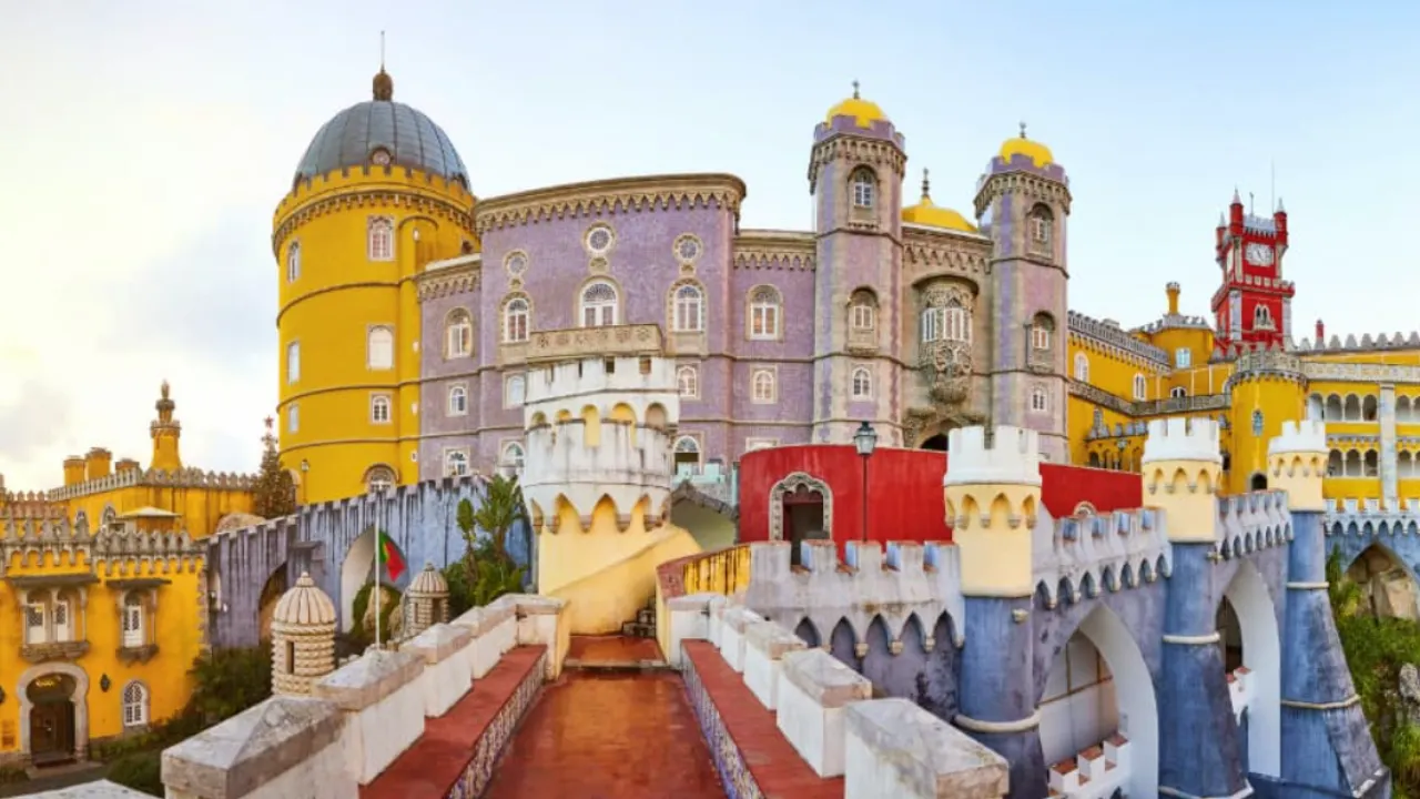 Voorkant van gekleurde gebouwen in vorm van kasteel van Sintra in Lissabon met blauwe lucht en zon op de achtergrond