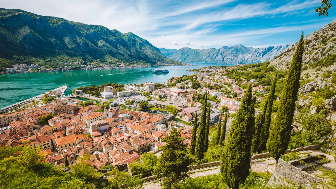 Geel/oranje huizen met op de voorgrond groene natuur en op de achtergrond review met blauw water en bergen