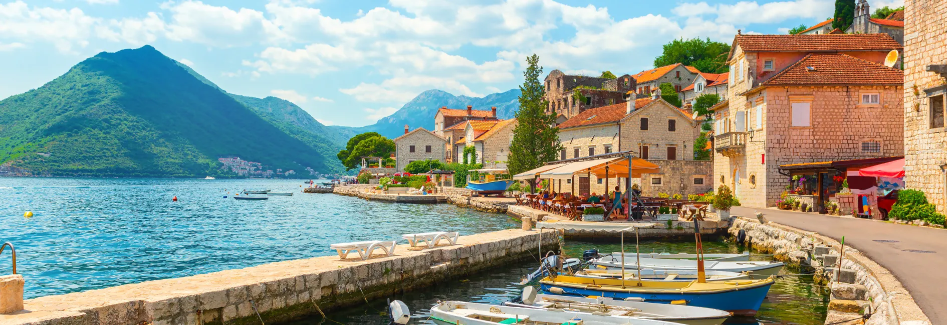 Wit/rode gebouwen aan het water met boten en met op de achtergrond bergen