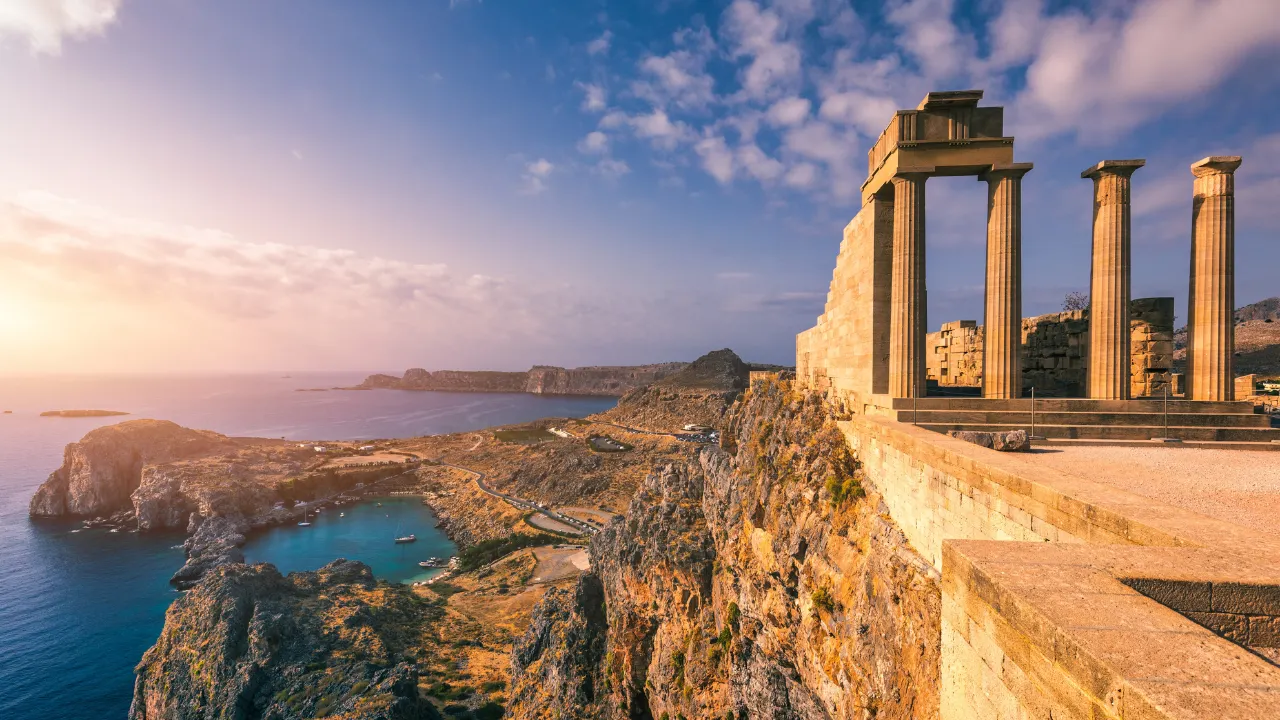 Zonsondergang boven Rhodos, Griekenland: Oude zuilen op een rots rechts, uitzicht op de kust links met blauwe zee en baaien. Perfect voor all-inclusive vakantie-ervaringen.