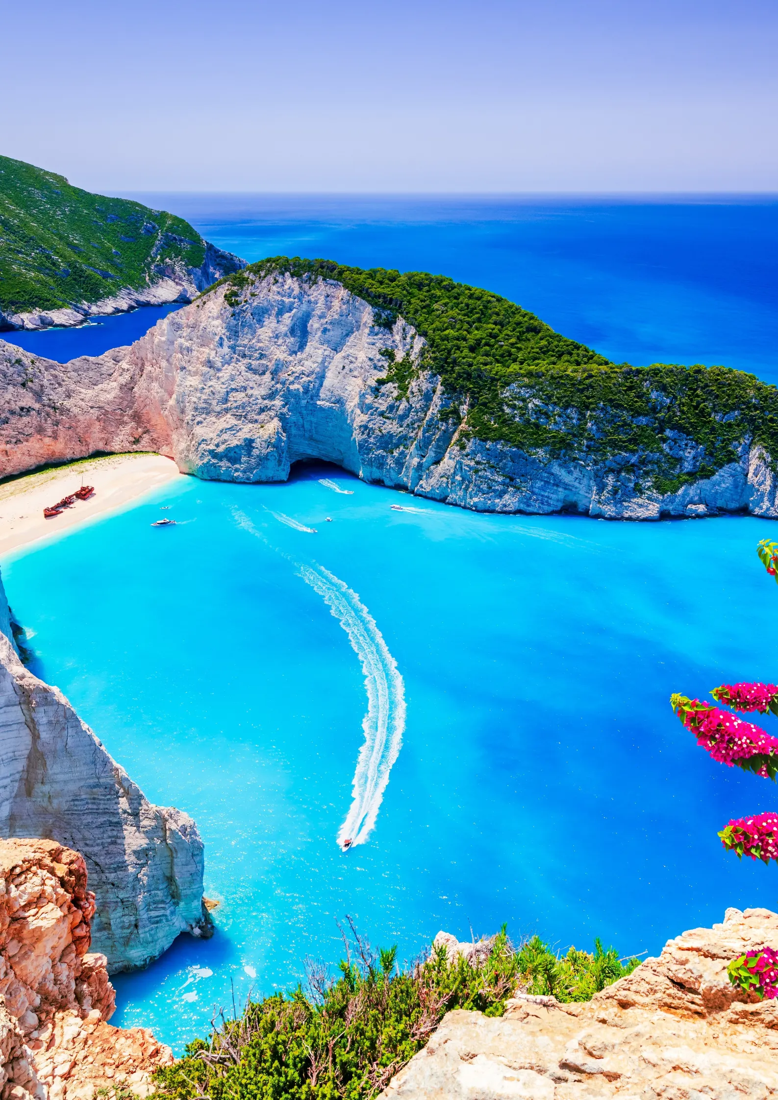 Spectaculair uitzicht op de turkooiskleurige Navagio-baai op Zakynthos met zijn witte zandstrand, steile kliffen, een roestig scheepswrak aan de linkerkant en passerende boten in het heldere water.