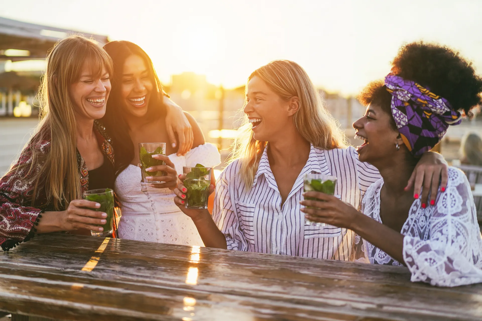 Vriendinnen lachen in een strandbar met cocktails in de hand