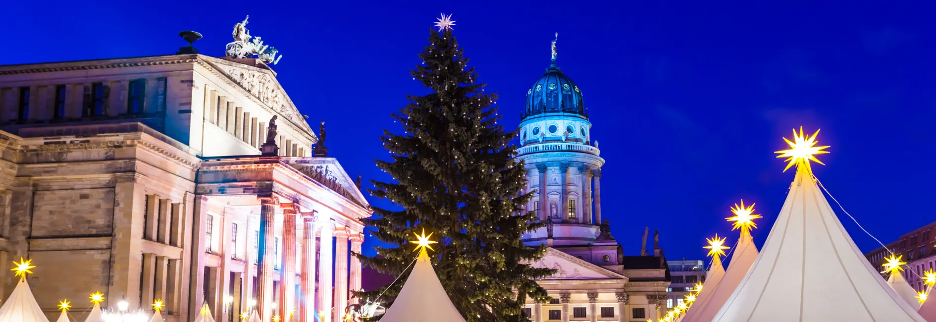 Grote kerstboom met sterpiek in het midden van een plein met historische gebouwen en kerstkraampjes met kerststerren