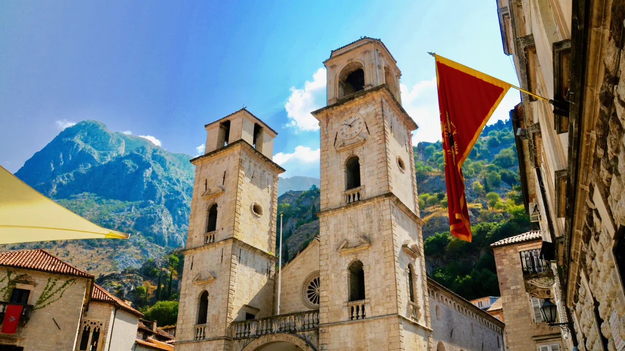 Kasteel met wit/gele stenen en zwarte details met op de achtergrond bergen en een blauwe lucht