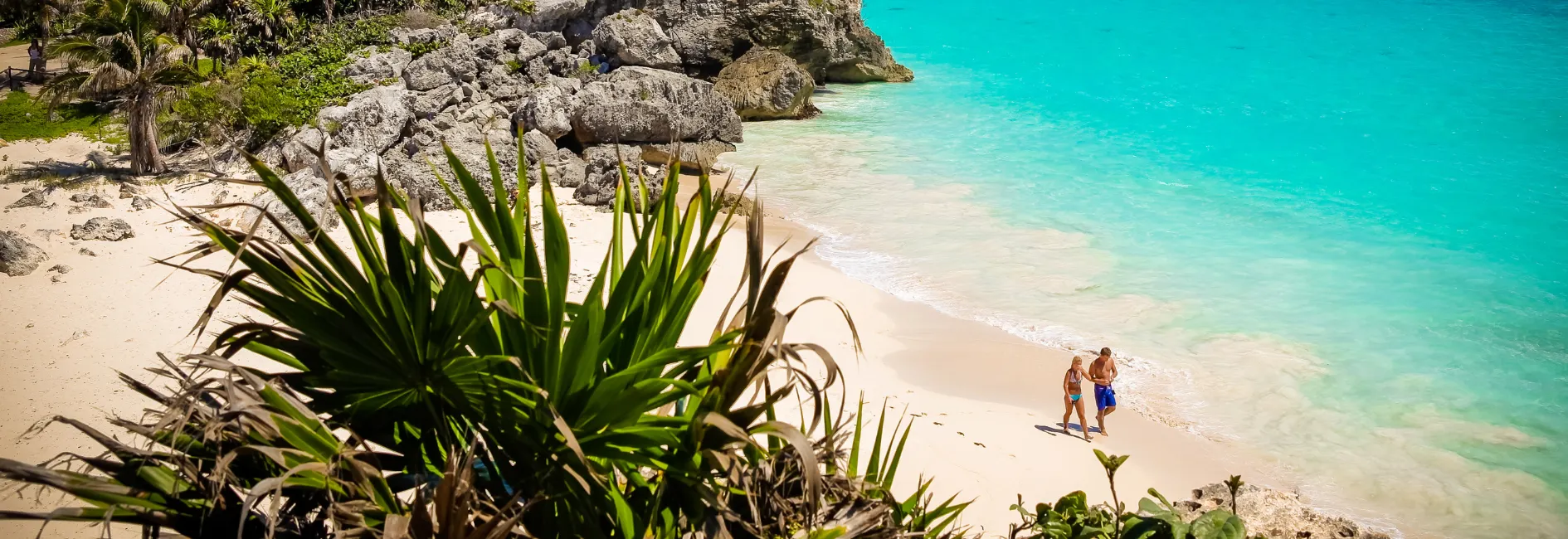 Foto van bovenaf van strand met blauw water en twee mensen die op strand lopen