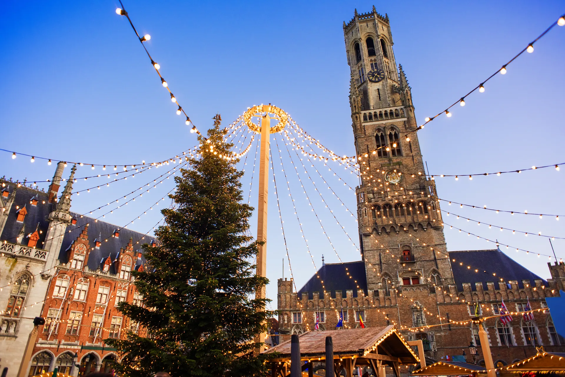 Kabelverlichting op plein met grote kerstboom en kerktoren