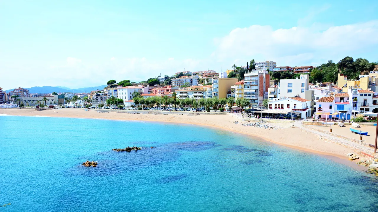 helder strand op Gran Canaria, turquoise water op de voorgrond, lichte huizen en bomen op de achtergrond
