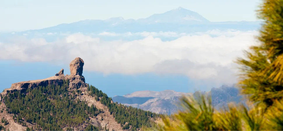 Rotsformatie op de top van een beboste berg op Gran Canaria, op de achtergrond meer bewolkte bergen
