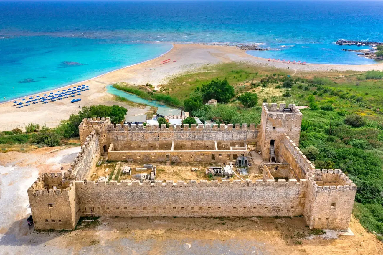 Oud kasteel met daarachter een strand met een helderblauwe zee en een groen landschap