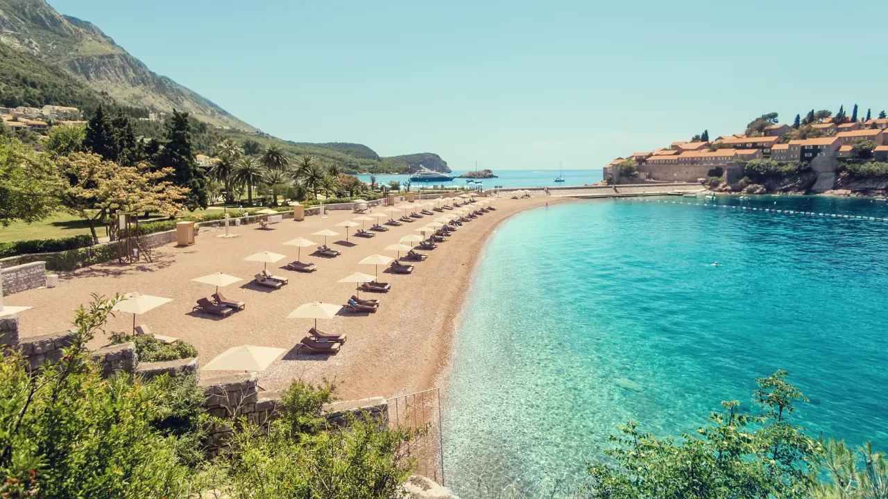 Zandstrand met om de voorgrond groene begroeiing en rechts van strand helderblauw water